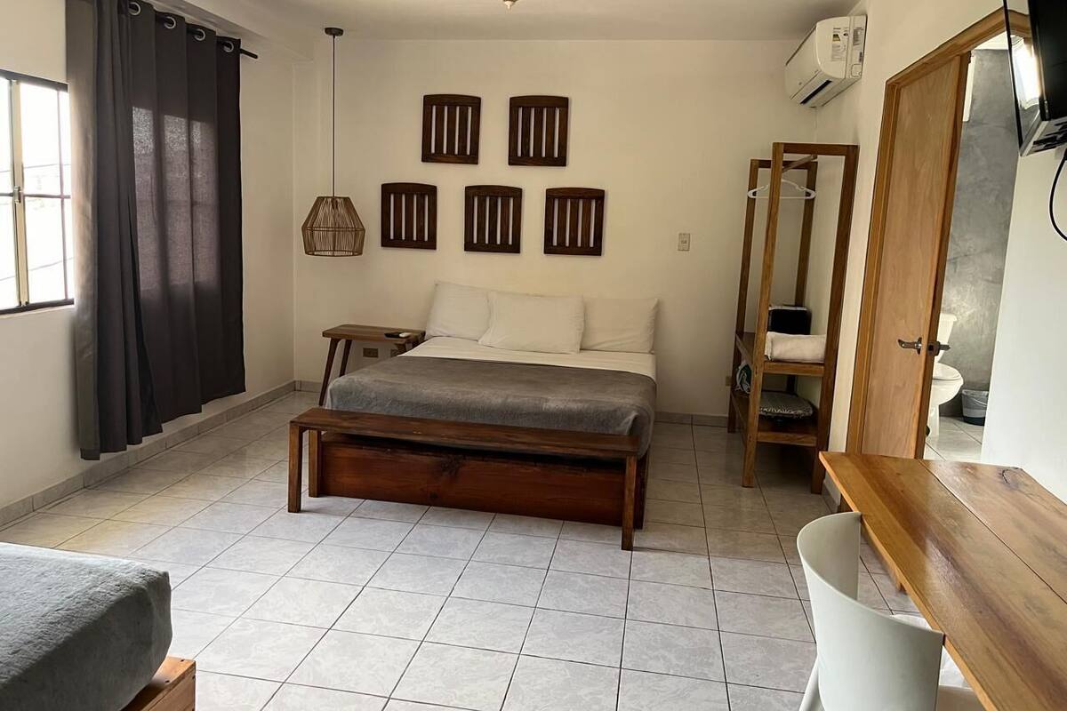 Ein Schlafzimmer mit Bett, einer hölzernen Bank, einem kleinen Tisch, einem Kleiderschrank und einem Spiegel.