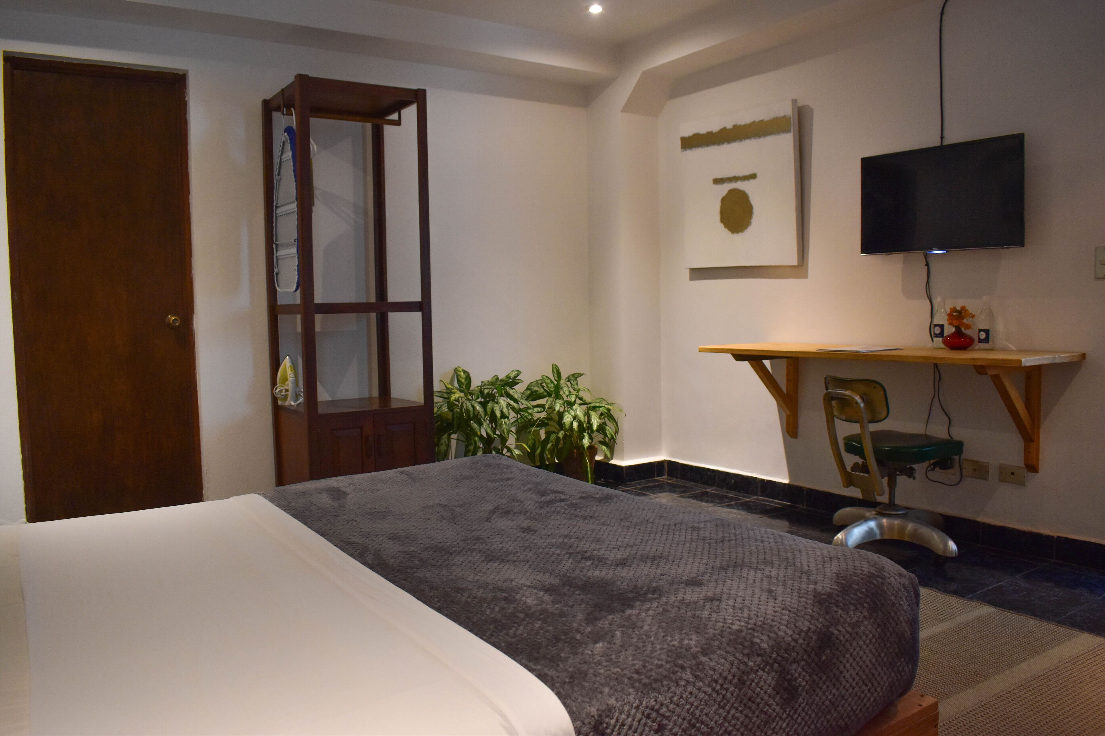 Un dormitorio con cama, escritorio, silla, televisor y puerta.