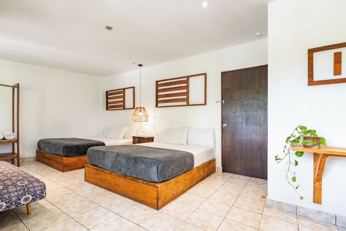 Ein Hotelzimmer mit zwei Betten, einer Holzbank, einem Nachttisch, einer Pendelleuchte und einem Blumentopf.