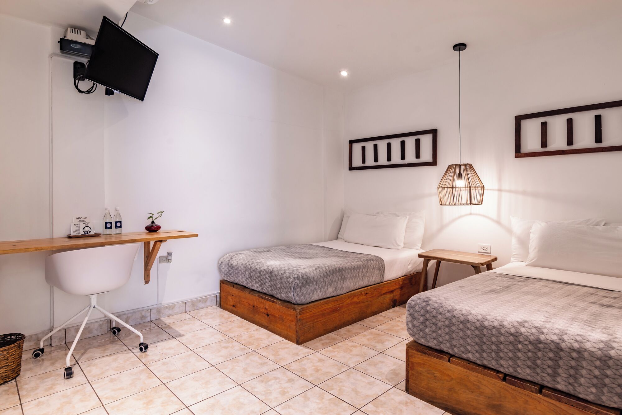 Een moderne slaapkamer met twee bedden, een bureau, een televisie en een klein tafeltje met een lamp.