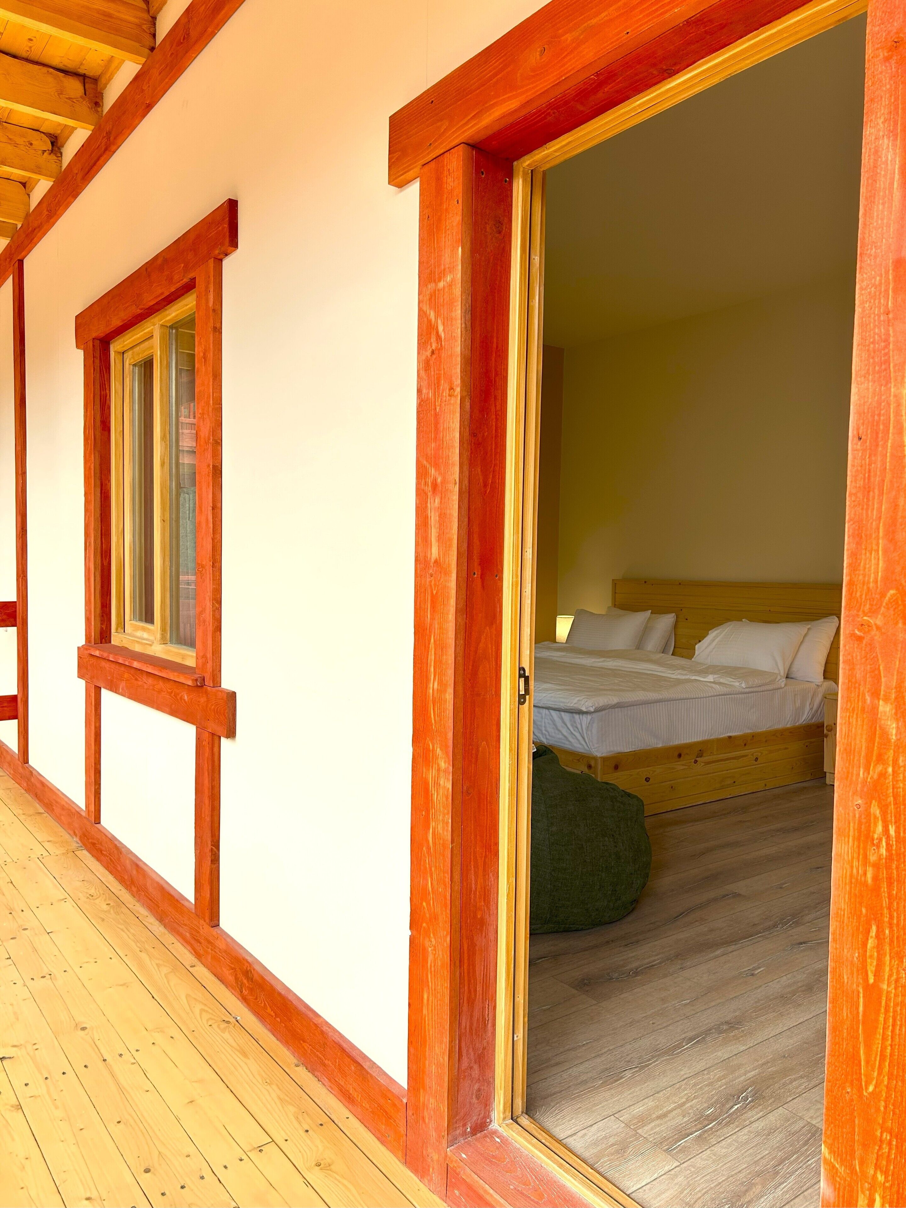 A wooden-framed room with a bed, a window, and a door leading to another room.