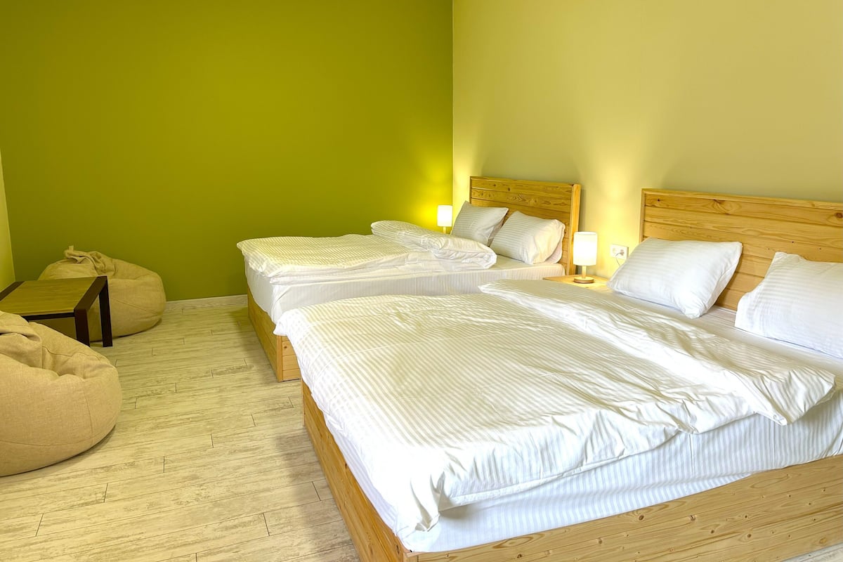 Een kamer met twee bedden, een houten hoofdbord, een nachtkastje met een lamp en een relax fauteuil.