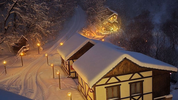 Un village enneigé, avec ses maisons traditionnelles en bois, un chemin de terre et des lampadaires.