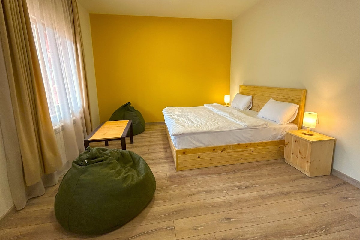 Een slaapkamer met een bed, nachtkastjes, een groene relaxfauteuil en een klein houten tafeltje.