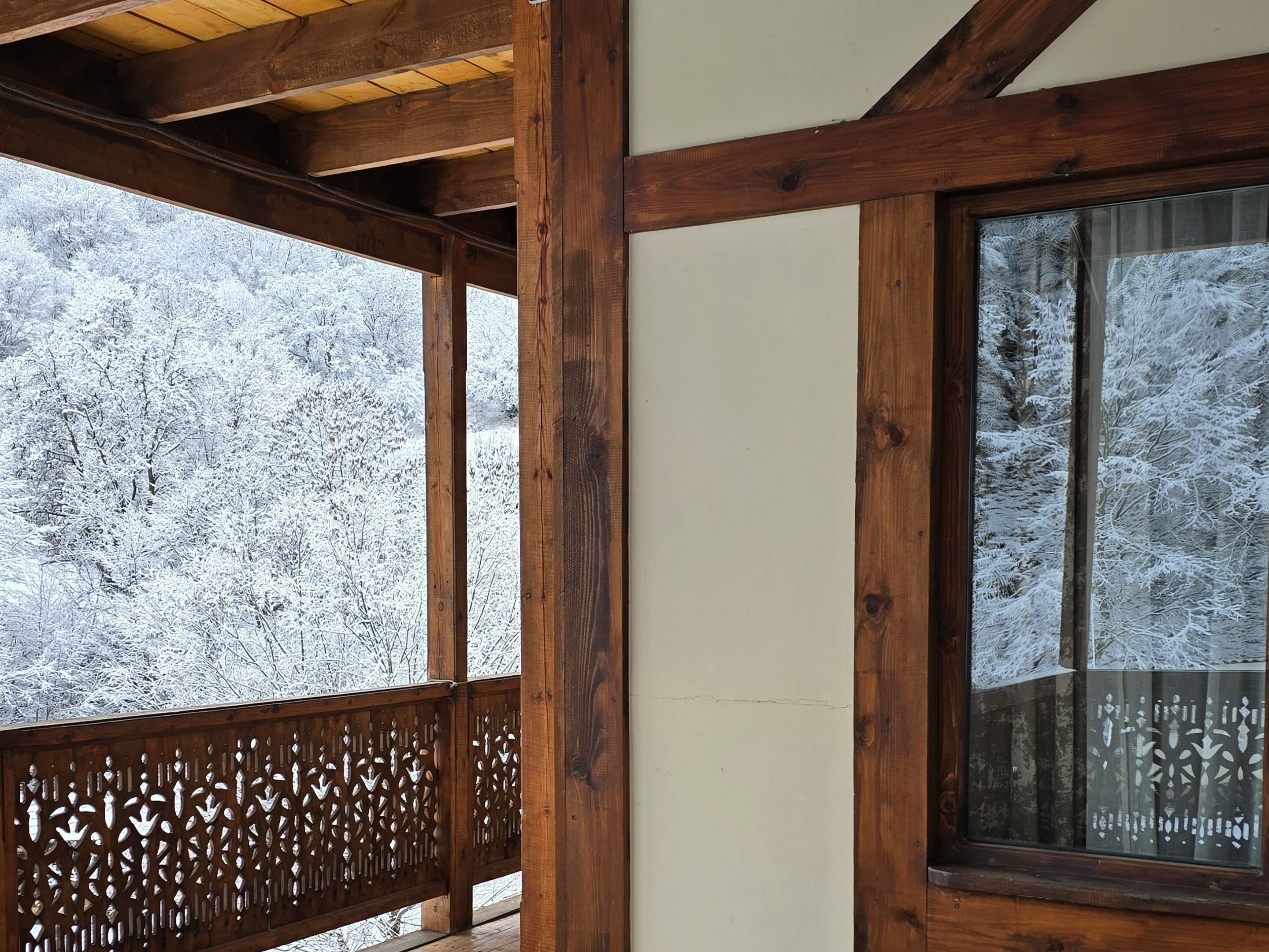 Un balcon en bois offrant une vue sur une forêt enneigée.