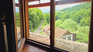 Une pièce dotée d’une grande fenêtre donnant sur un paysage pittoresque, avec une route et des bâtiments traditionnels.