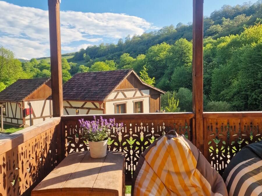 Una terraza de madera con vistas a casas tradicionales de entramado y abundante vegetación al fondo.