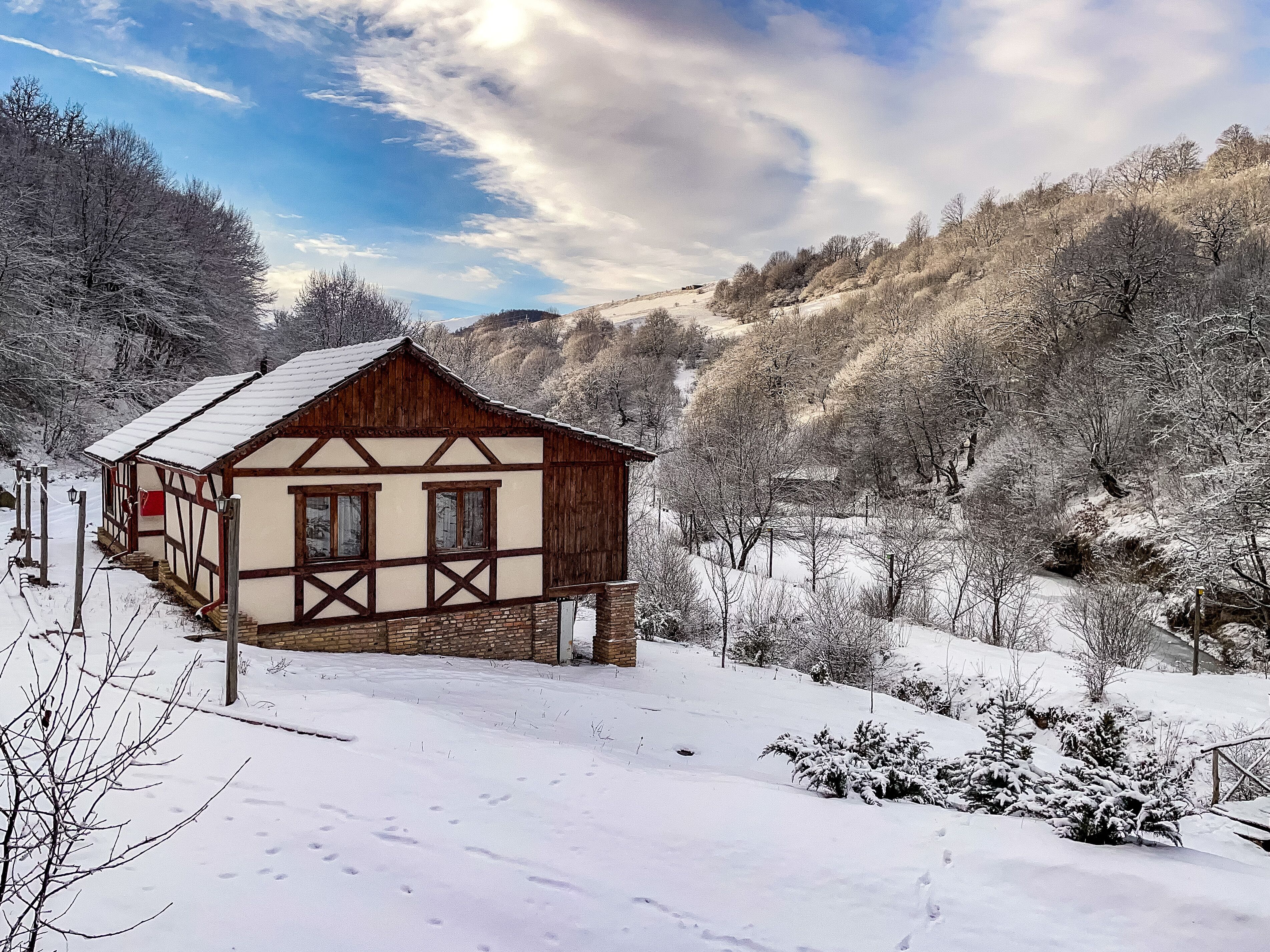 A traditional half-timbered house with a sloped roof, surrounded by snow-covered trees and hills.
