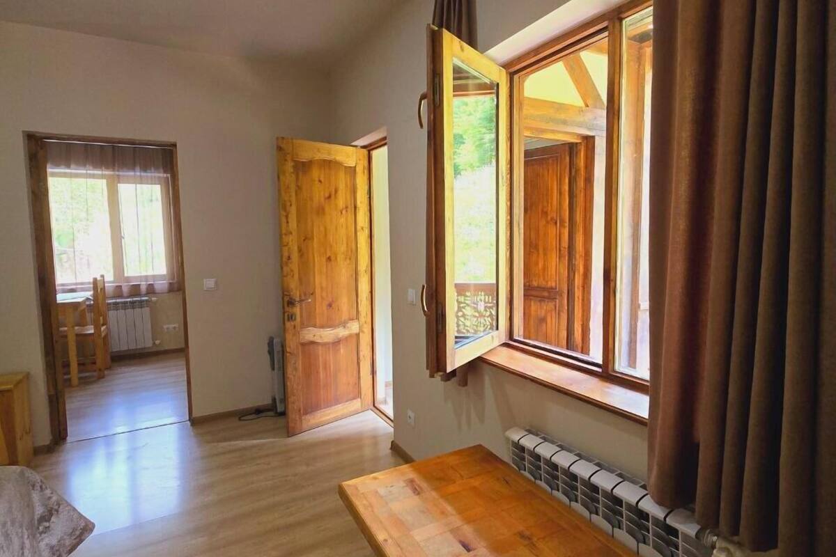 Een ruime kamer met houten vloeren, een groot raam met gordijnen en een houten tafel.