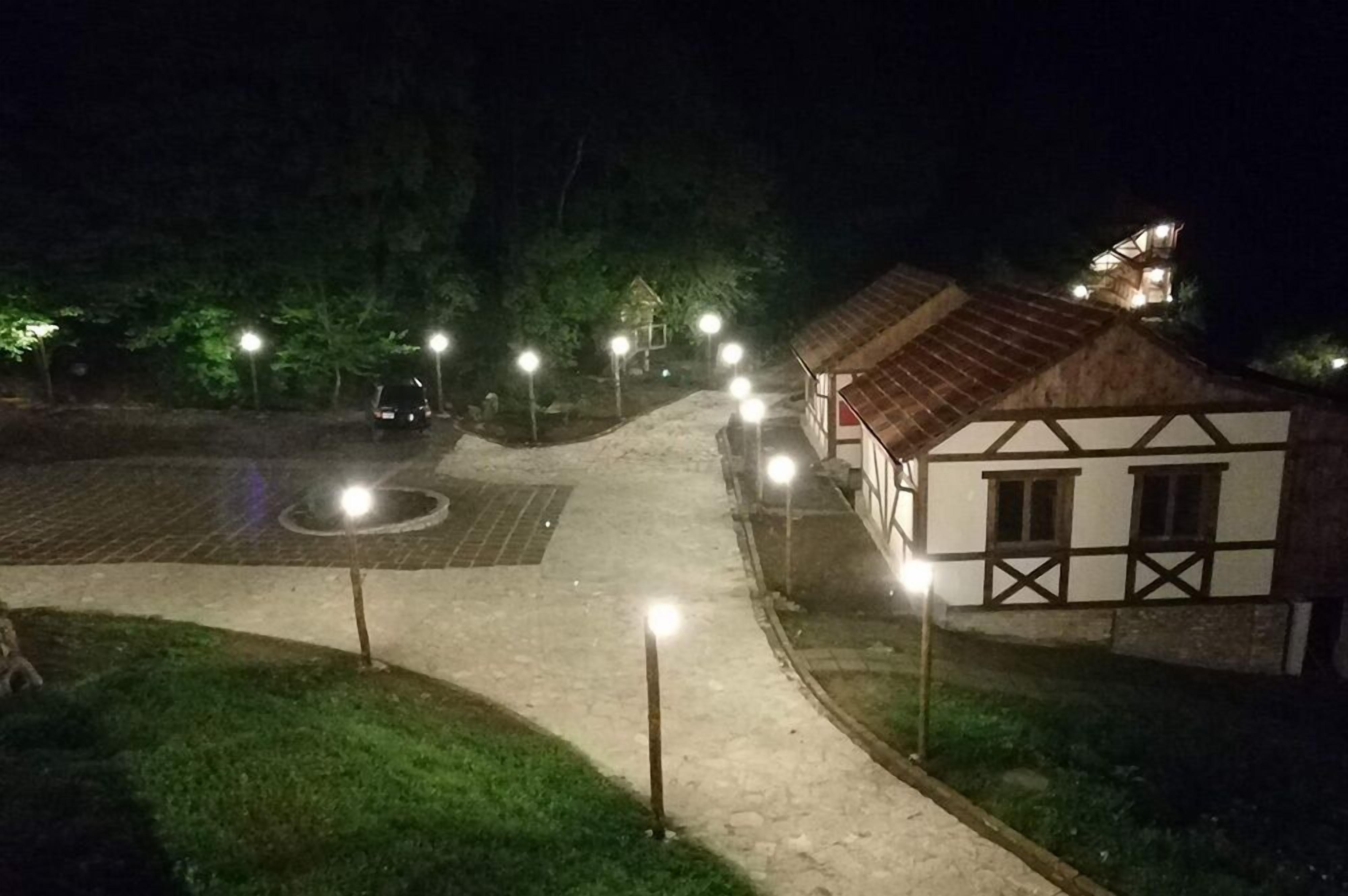 Vista nocturna de un edificio de estilo arquitectónico tradicional, con un acceso empedrado y árboles circundantes.