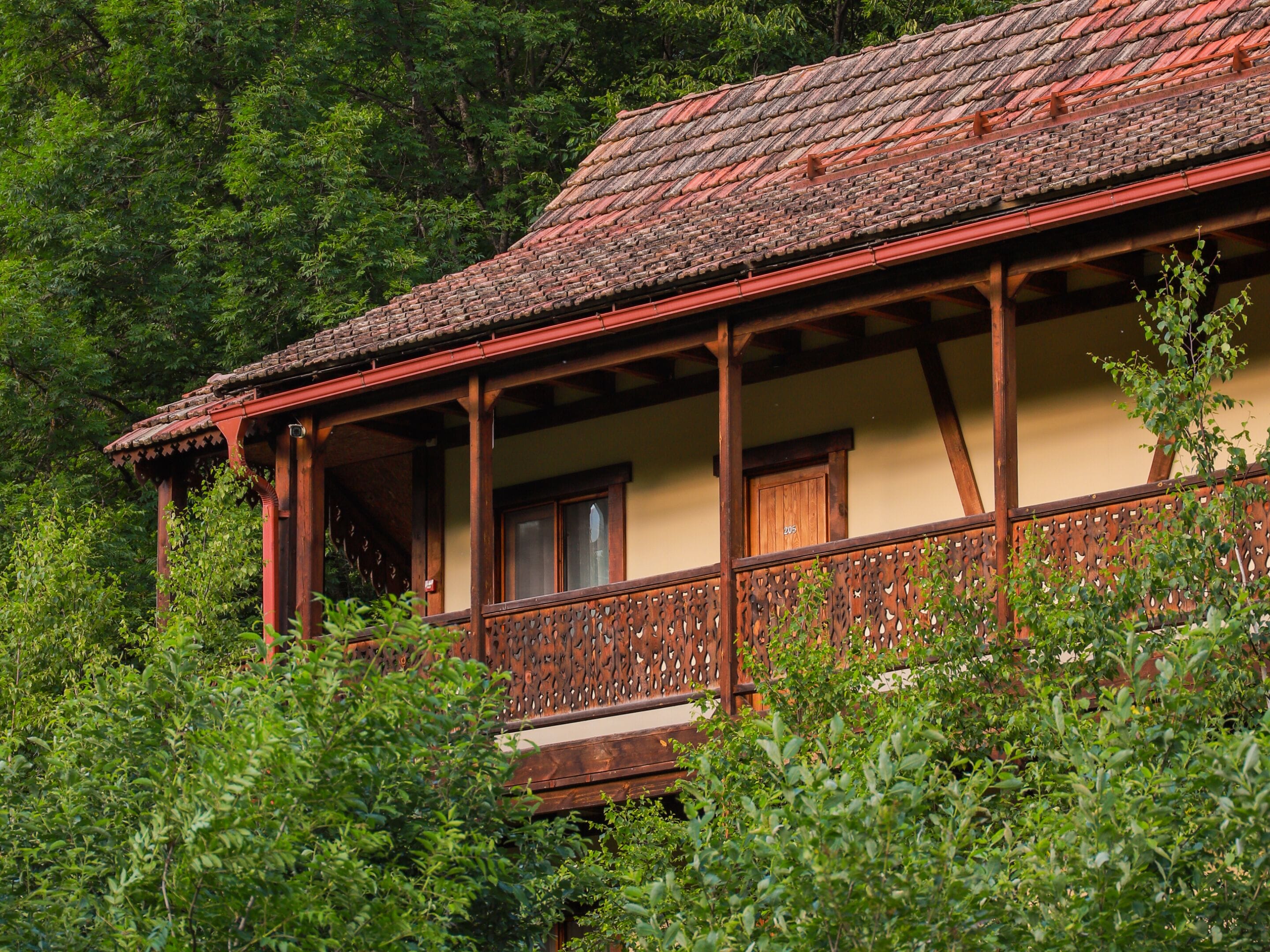 A traditional wooden house with a balcony, surrounded by dense greenery.