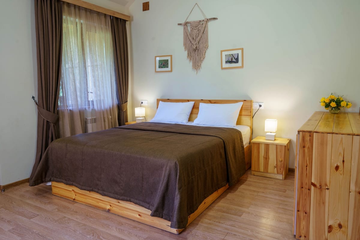 Een keurig opgemaakt slaapkamer met een houten bed, twee nachtkastjes met lampen, een houten kast en een macramé wanddecoratie.