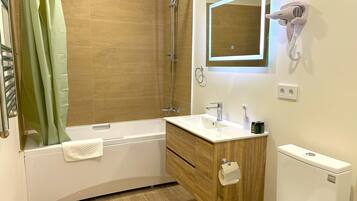 Une salle de bain moderne avec un plancher en bois, une baignoire blanche, un meuble-lavabo en bois, un miroir, un sèche-cheveux et des toilettes.