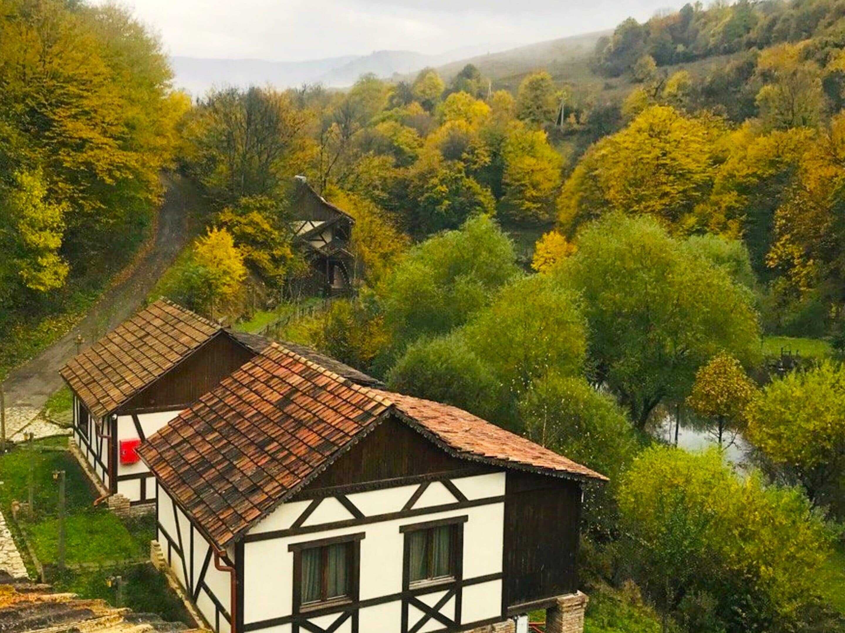 A traditional half-timbered house with a sloped roof, surrounded by lush greenery and a river.
