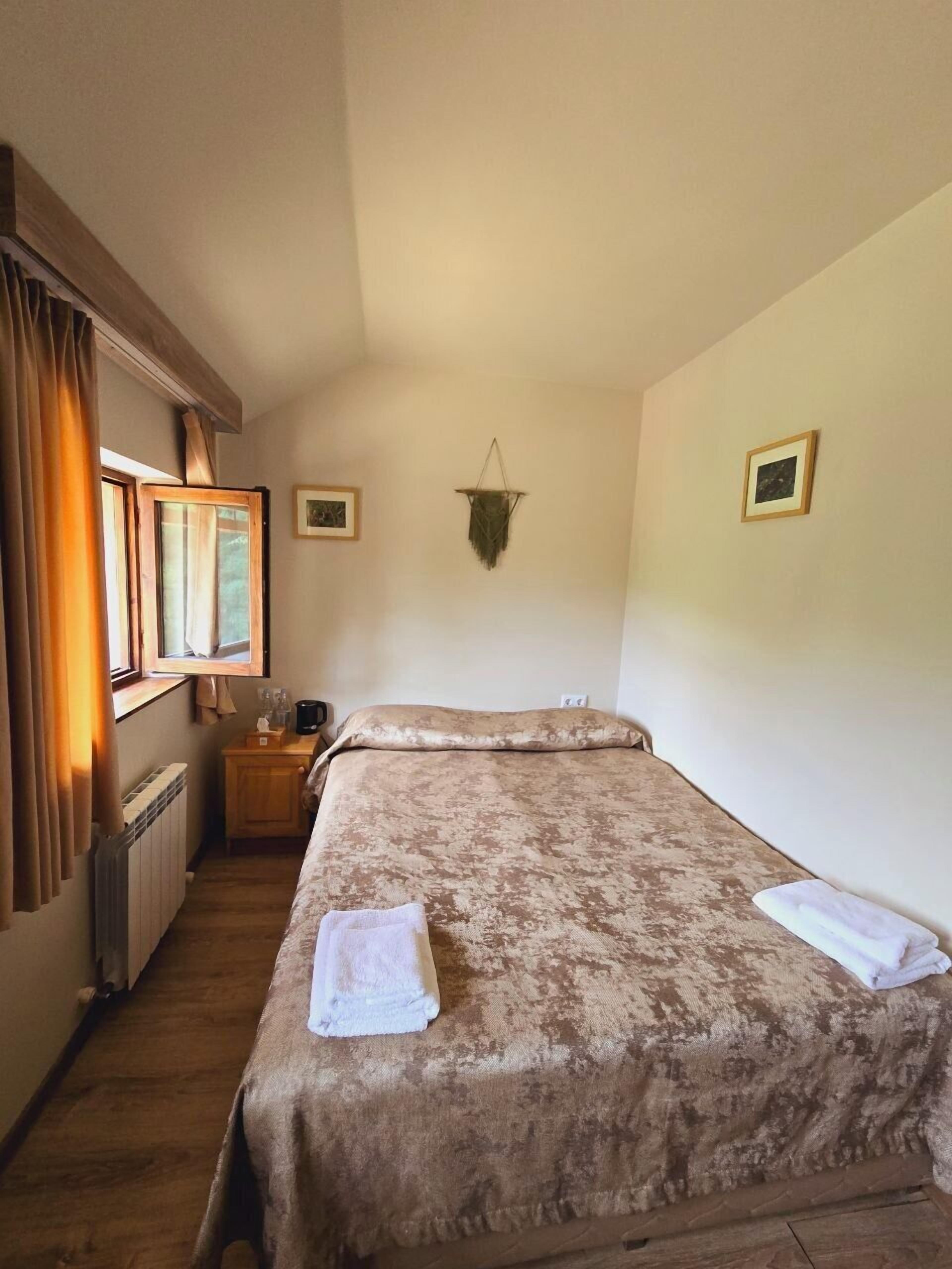 A bedroom with a bed, a nightstand, a window with curtains, a radiator, and a wall-mounted decoration.