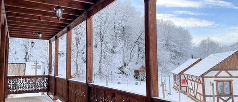 A wooden balcony with a view of snow-covered trees and buildings.