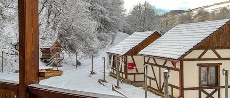 Una cabaña de madera con techo nevado y una terraza de madera.