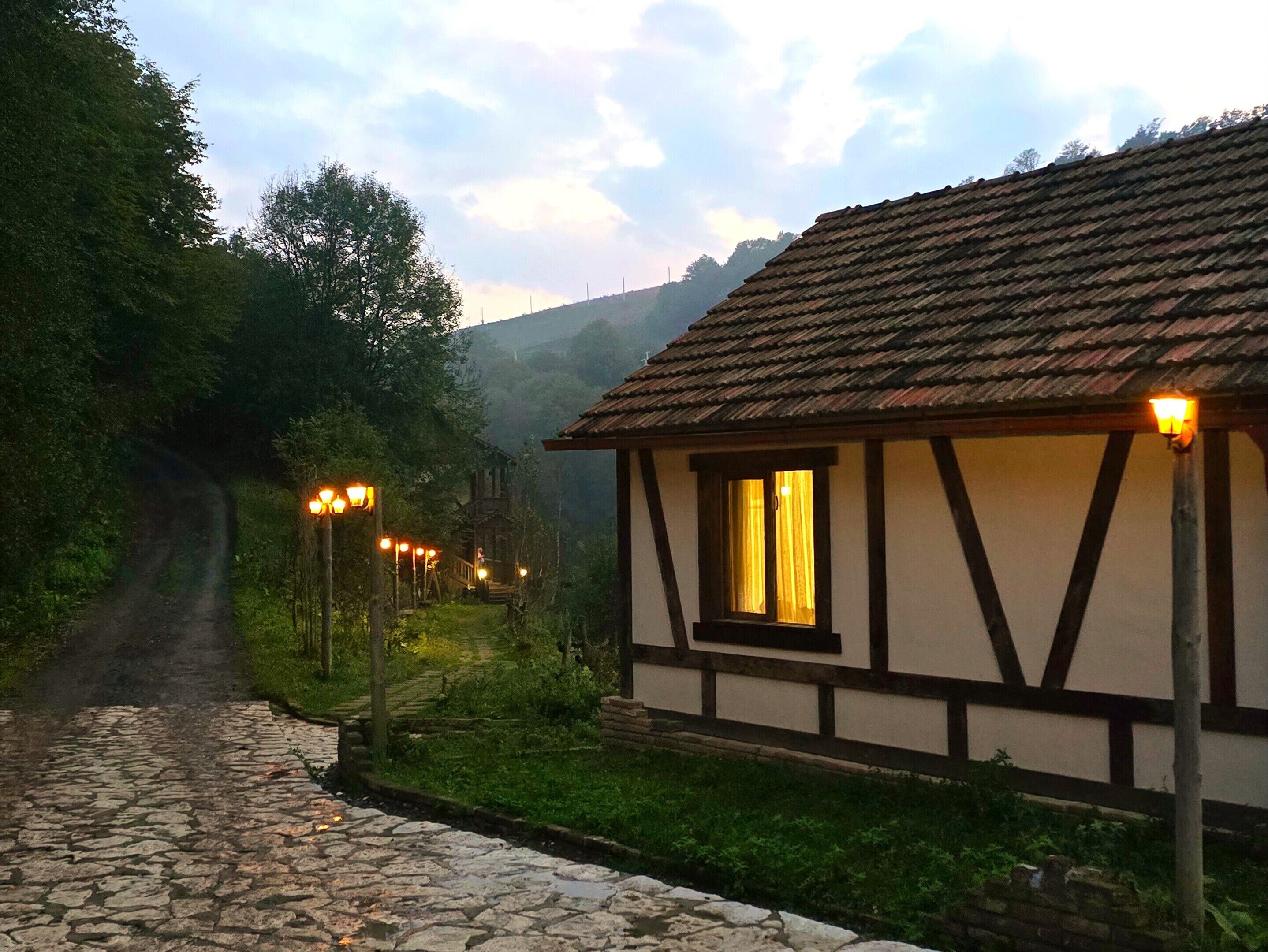 Una casa tradicional de entramado de madera con un sendero de piedra que la conduce, rodeada de vegetación y colinas.