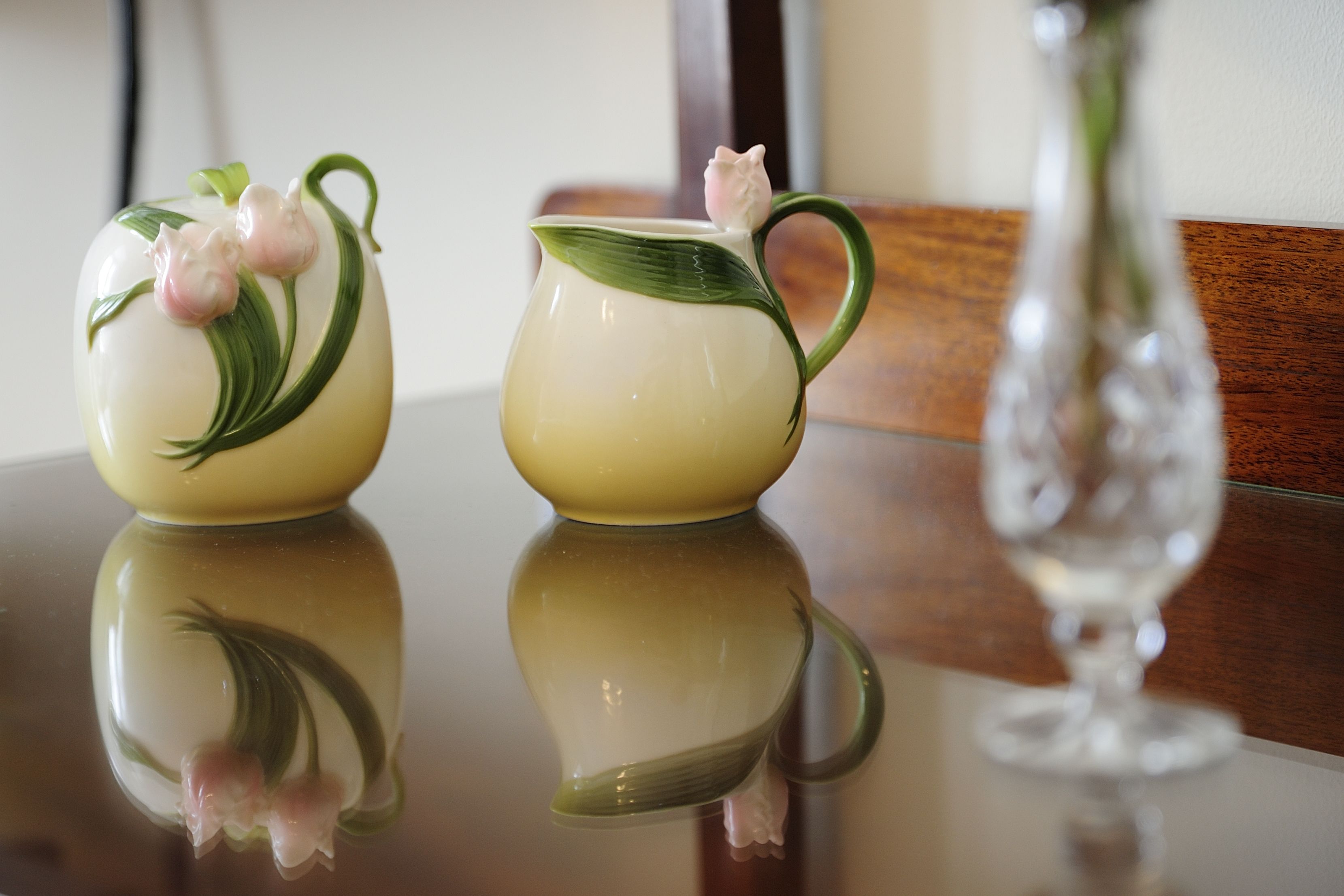 Two ceramic pitchers with floral designs on a reflective surface.