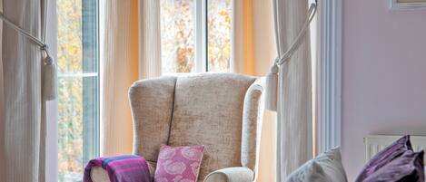 A room with a large armchair, a bed with a white duvet, and a window with curtains.