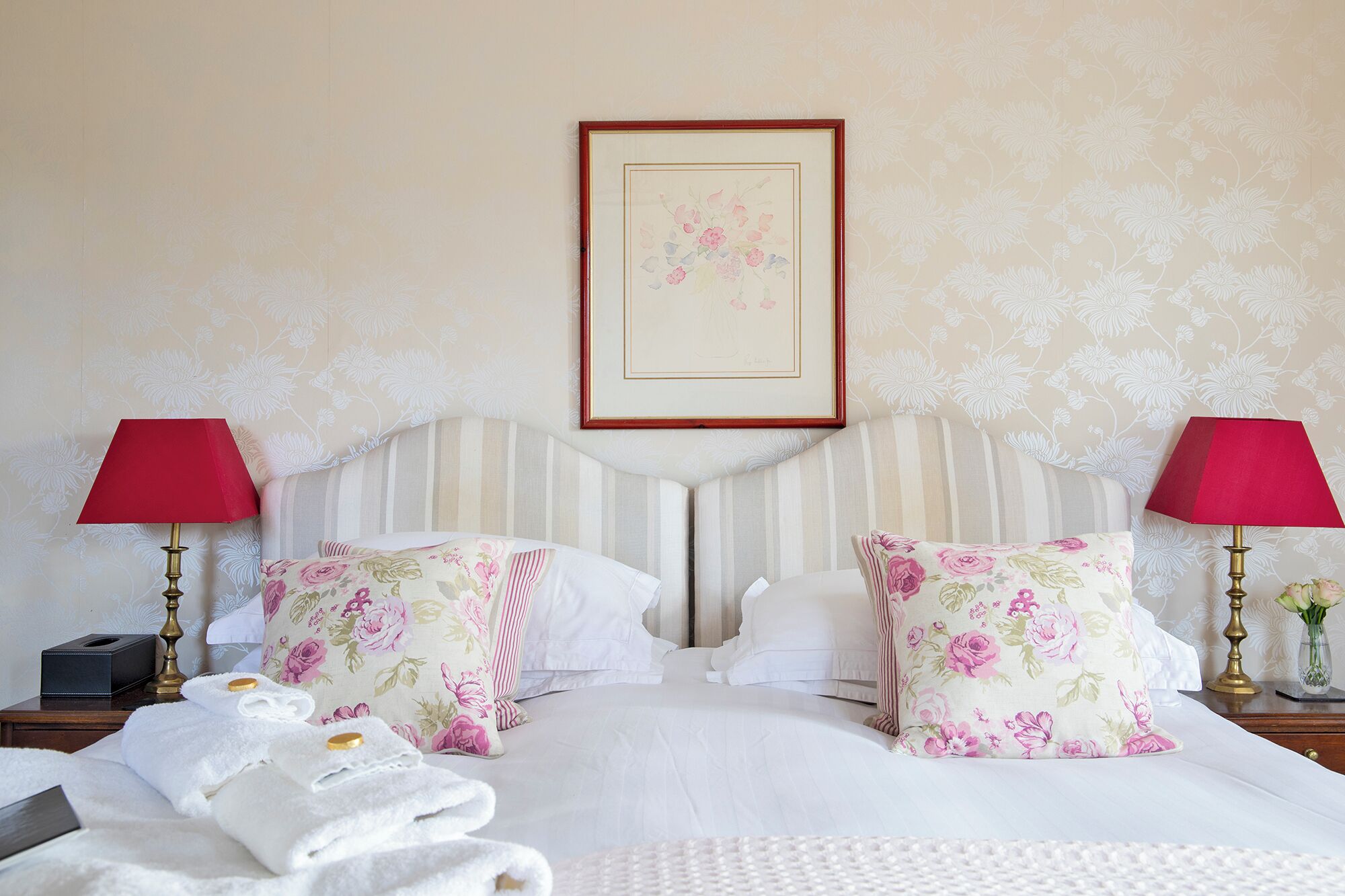 A neatly made bed with floral pillows, two bedside lamps, and a framed floral artwork on the wall.