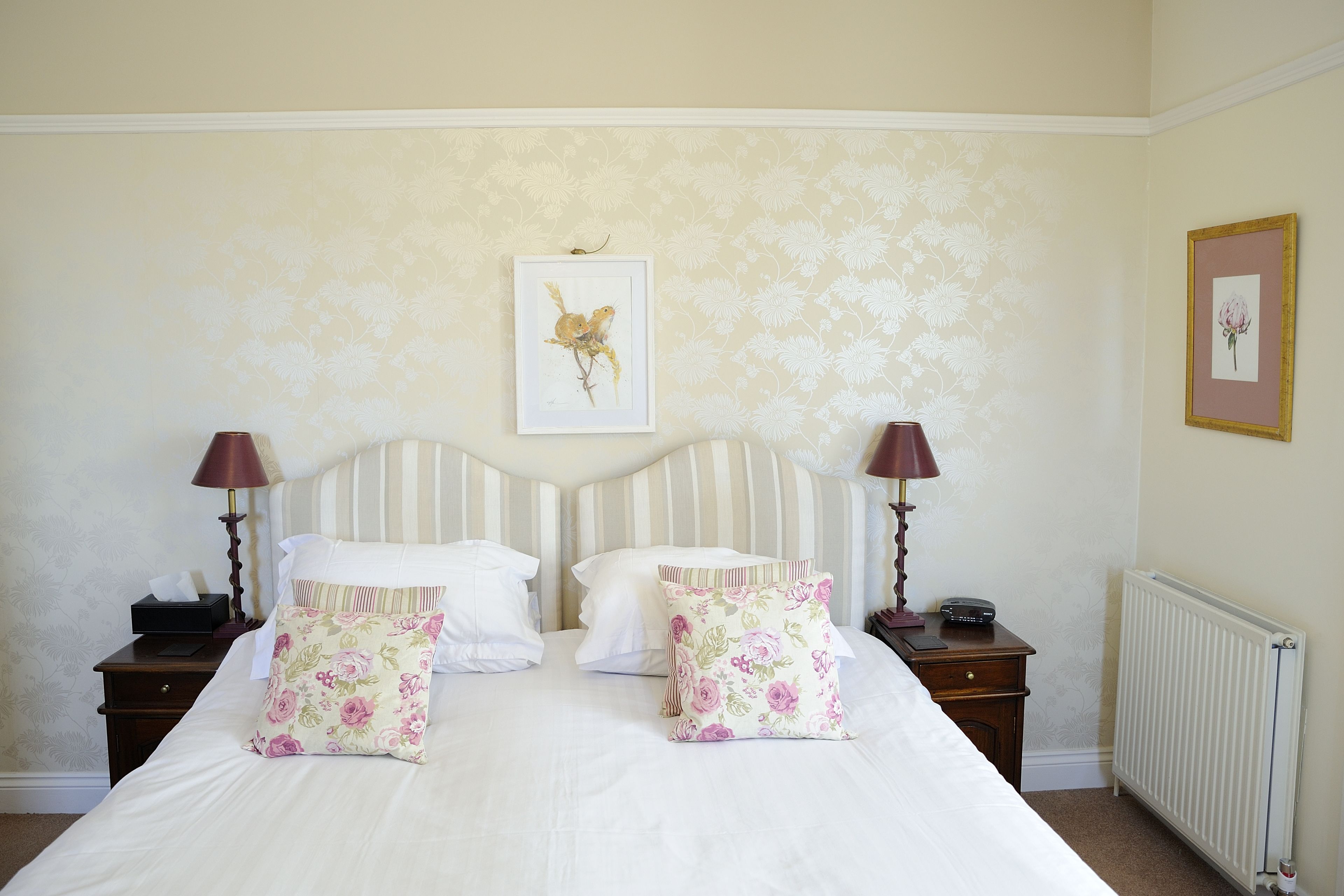 A neatly made bed with floral pillows, a striped headboard, and two bedside tables with lamps.