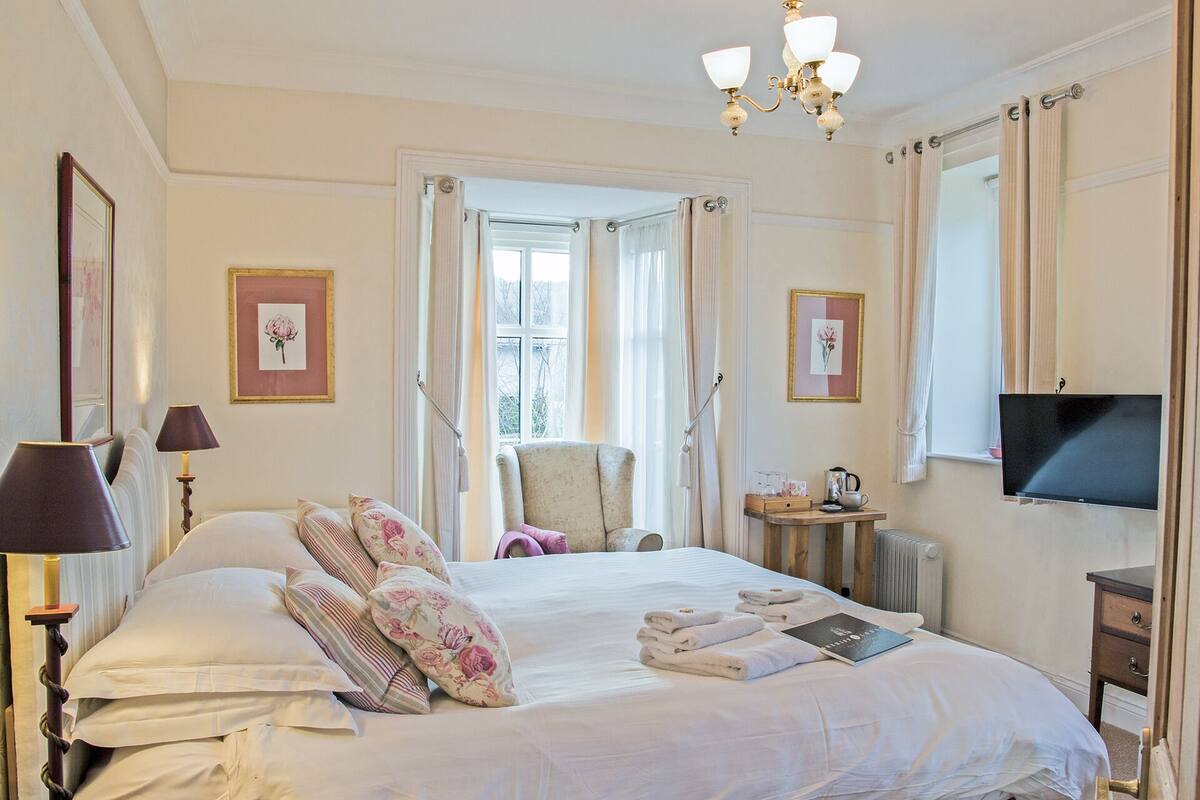 A hotel room with a bed, a chair, a TV, and a window with curtains.