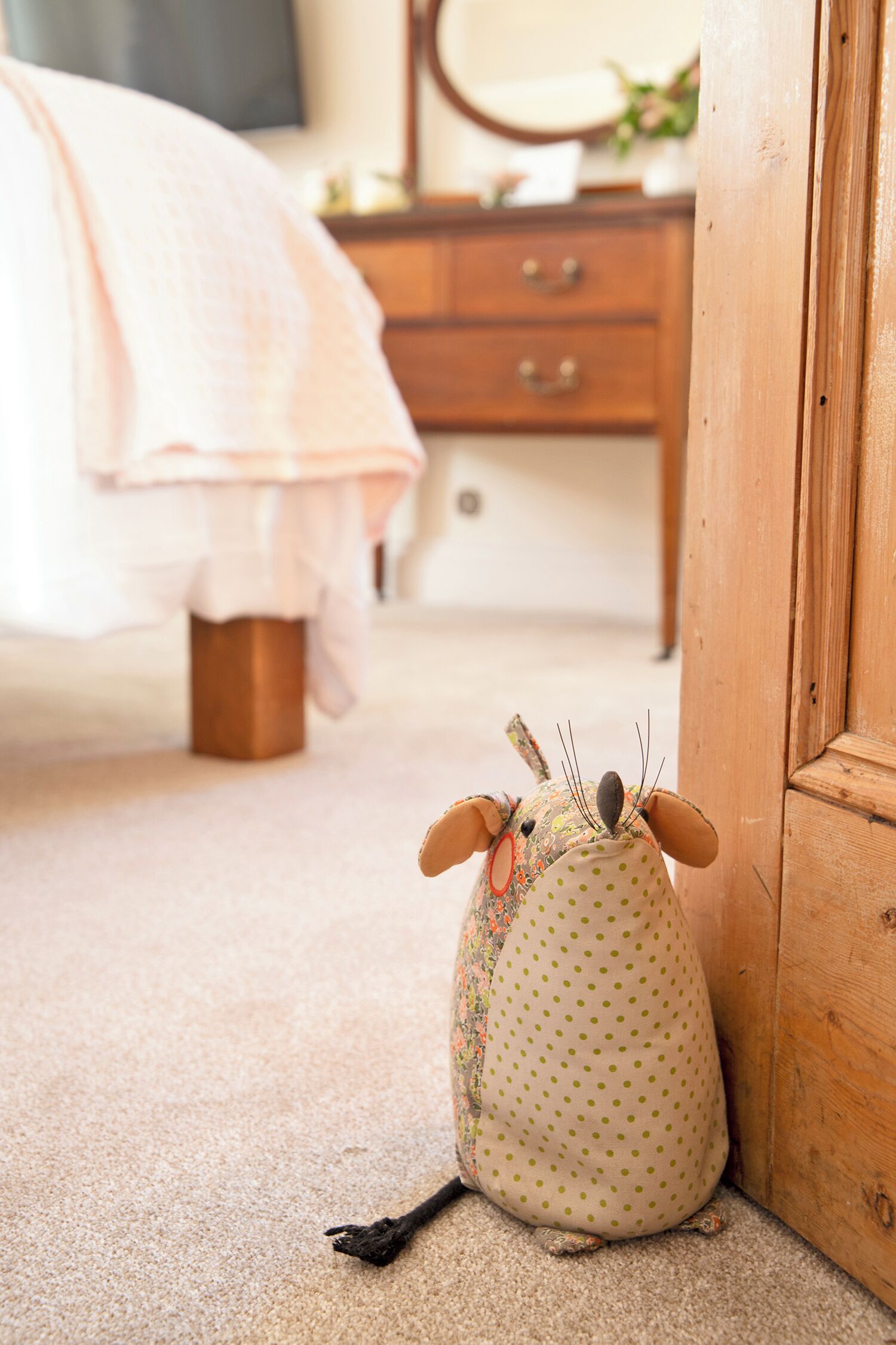 A plush toy with a polka dot pattern and a brown base, positioned on a carpeted floor next to a wooden door.