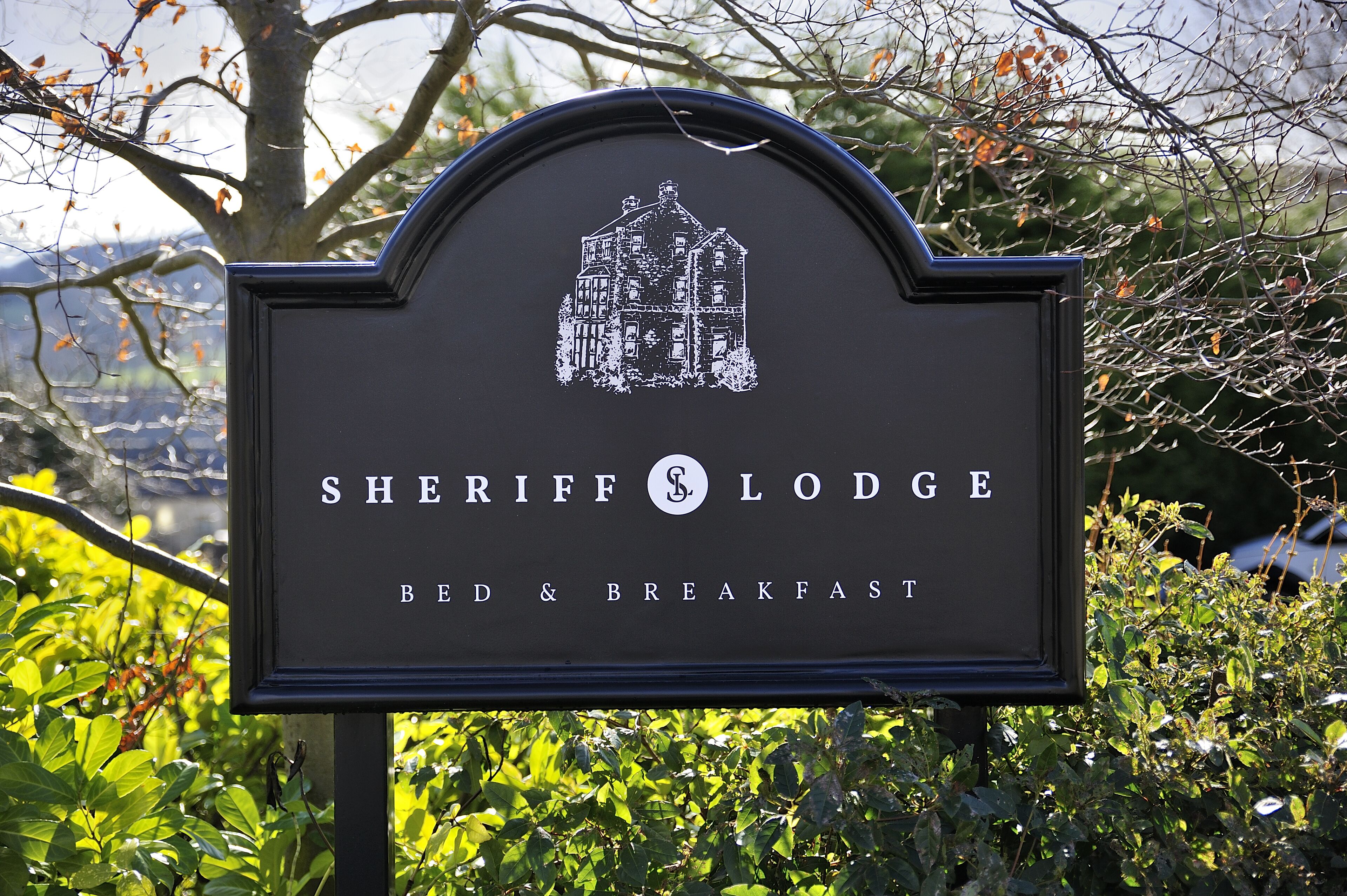 A sign for Sheriff Lodge Bed & Breakfast with a house illustration.