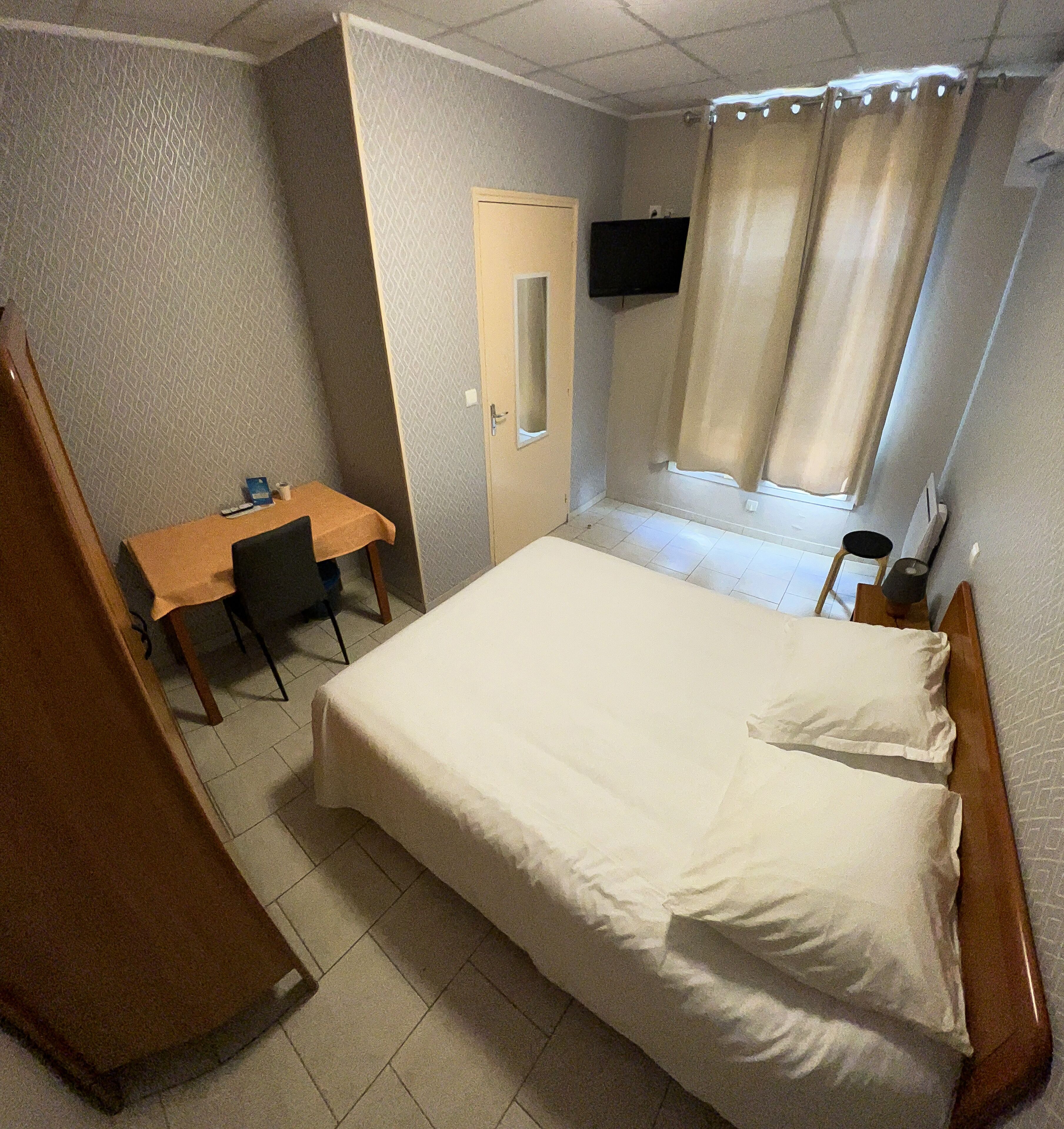 Hotellihuone, jossa on sänky, työpöytä, tuoli, televisio ja ikkuna, jossa on verhot.