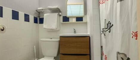 Un baño pequeño con inodoro, lavamanos con espejo y cortina de ducha con caracteres chinos.