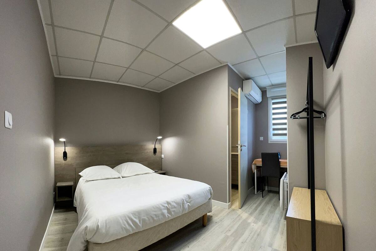 Une chambre à coucher avec un lit, des lampes de chevet, un bureau et un téléviseur.