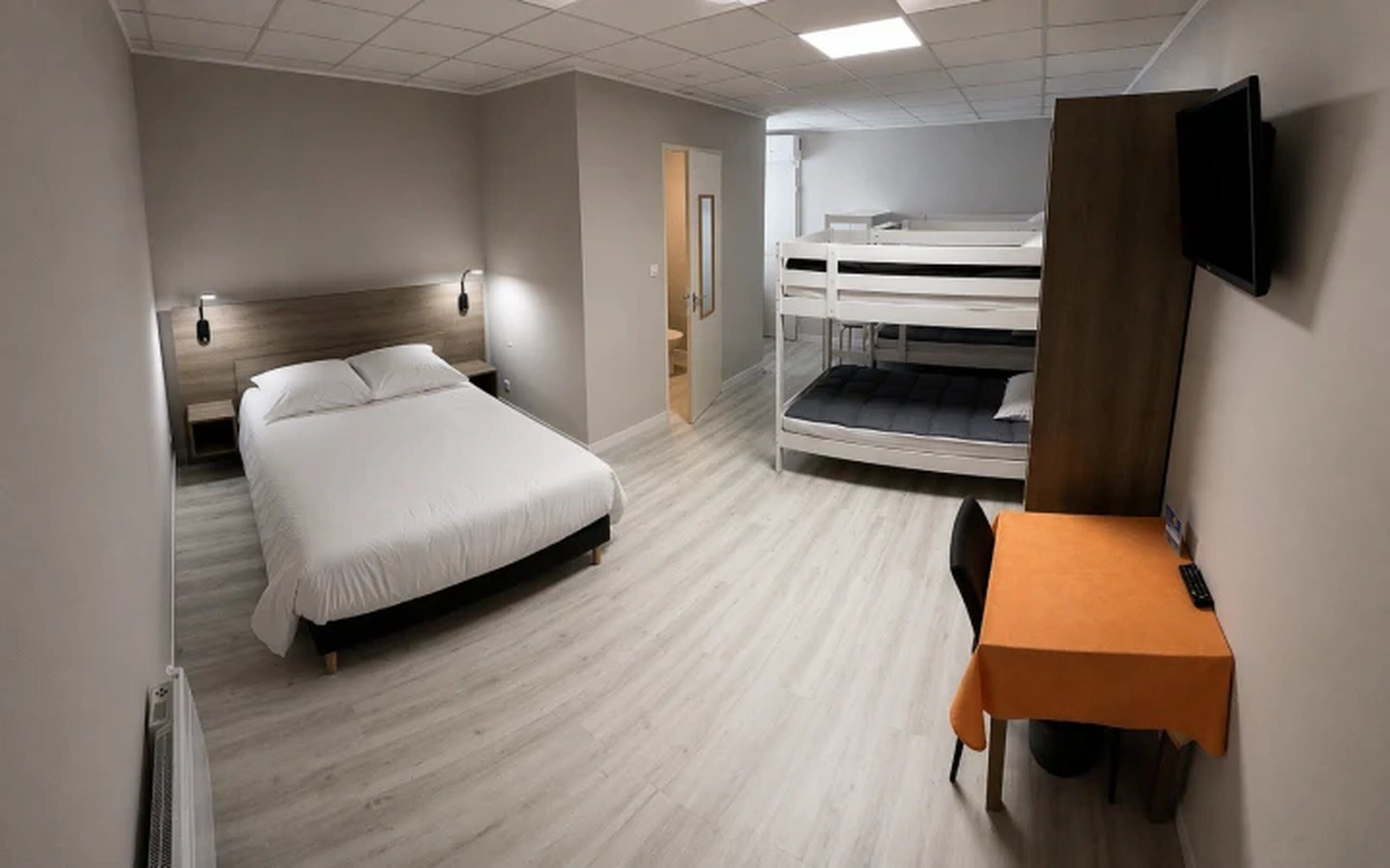 Ett hotellrum med en enkelsäng, ett skrivbord, en stol, en våningssäng och en TV.