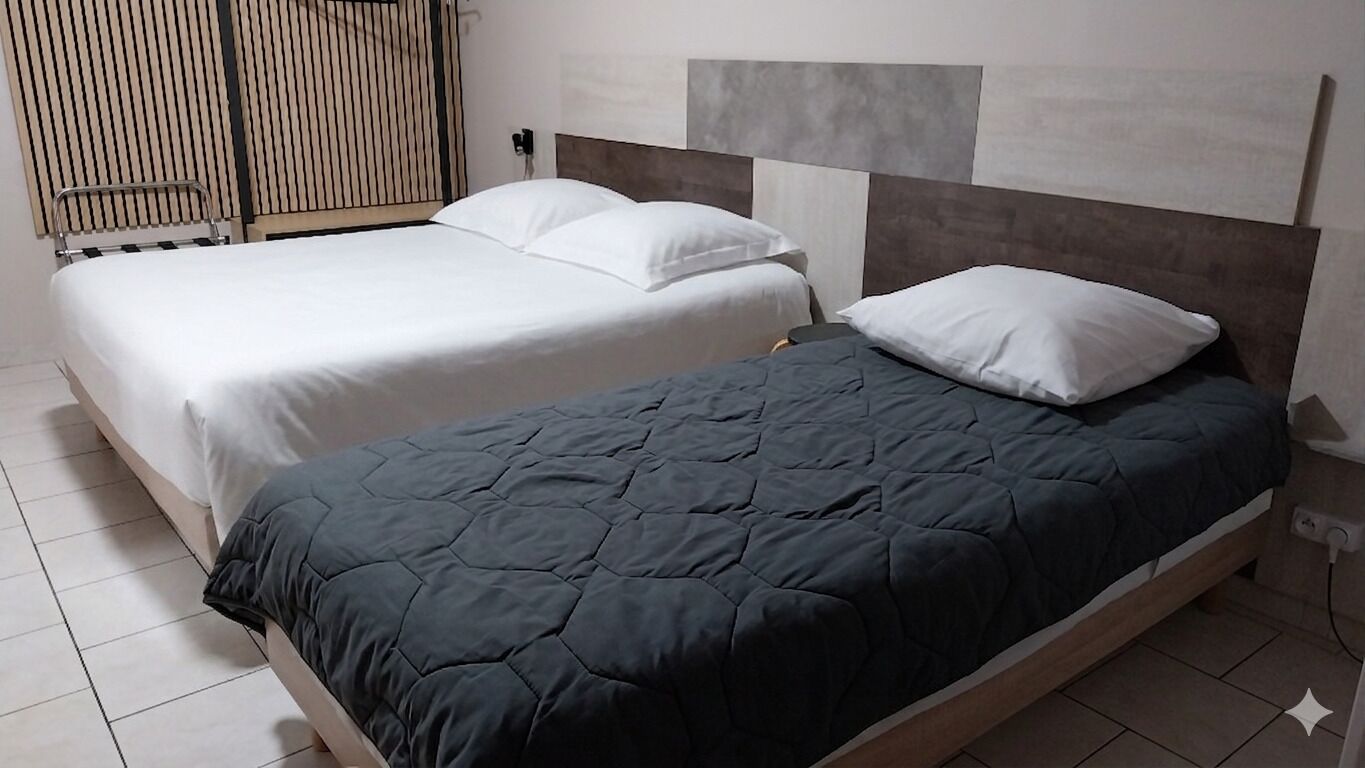 A hotel room with two beds, one with a white bedspread and the other with a dark quilted bedspread.