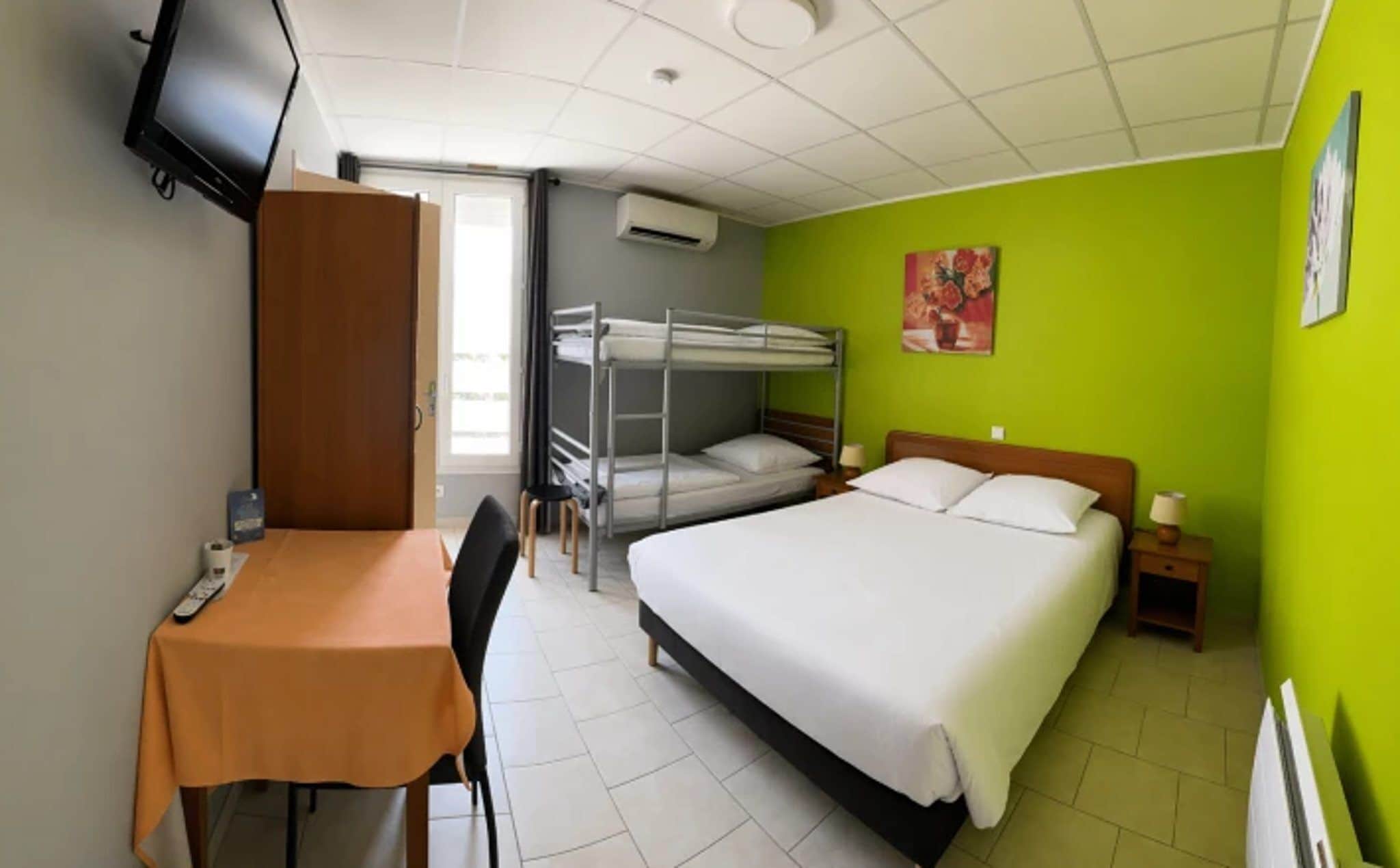 Una habitación con literas, un escritorio con silla, un televisor y un cuadro en la pared.