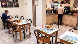 Un comedor con mesas, sillas y una zona de cocina con cafetera.