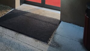 Entrada de hotel con puerta de vidrio, alfombra roja y una planta en maceta en el interior.