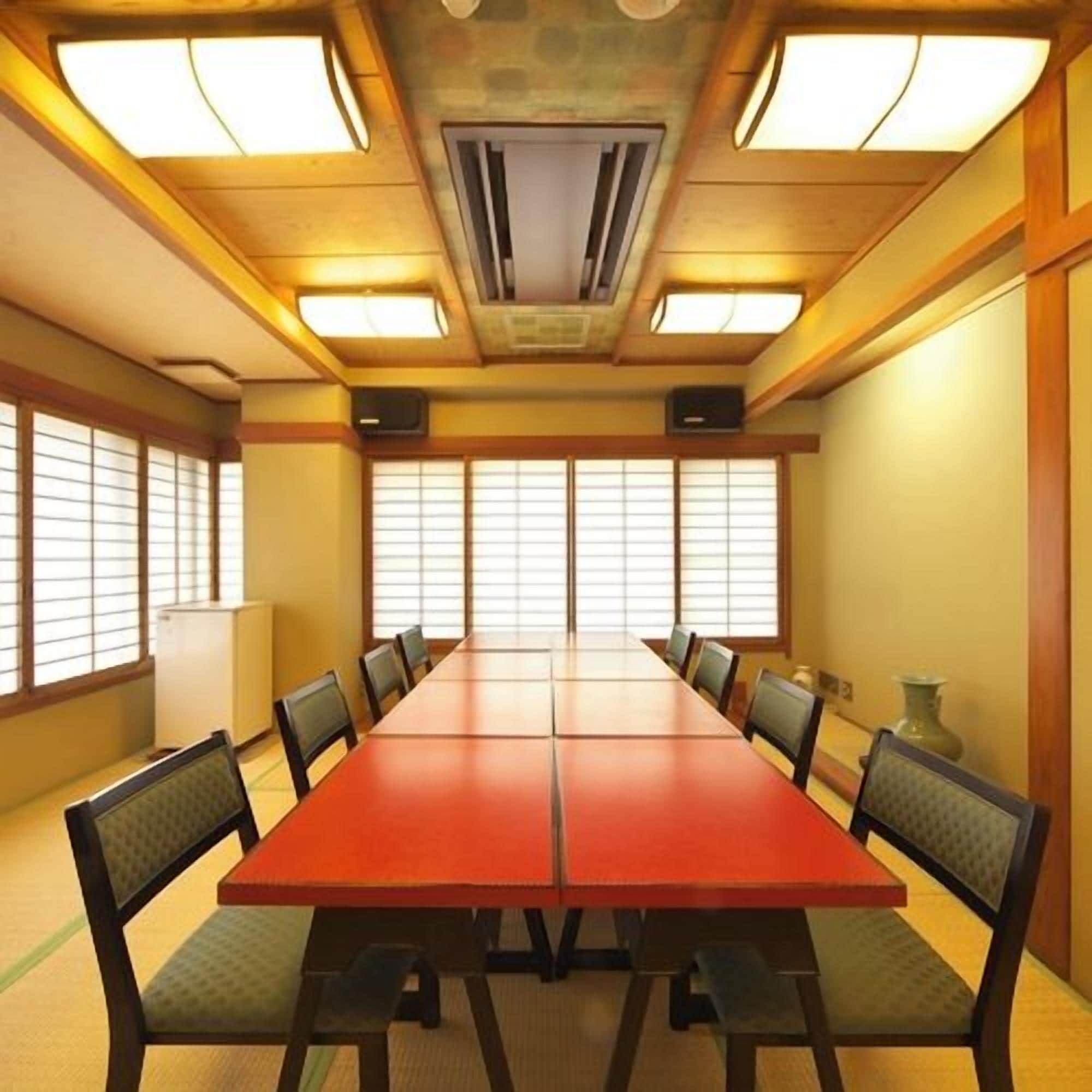 A conference room with a long table and chairs, large windows with blinds, and a ceiling with recessed lighting.