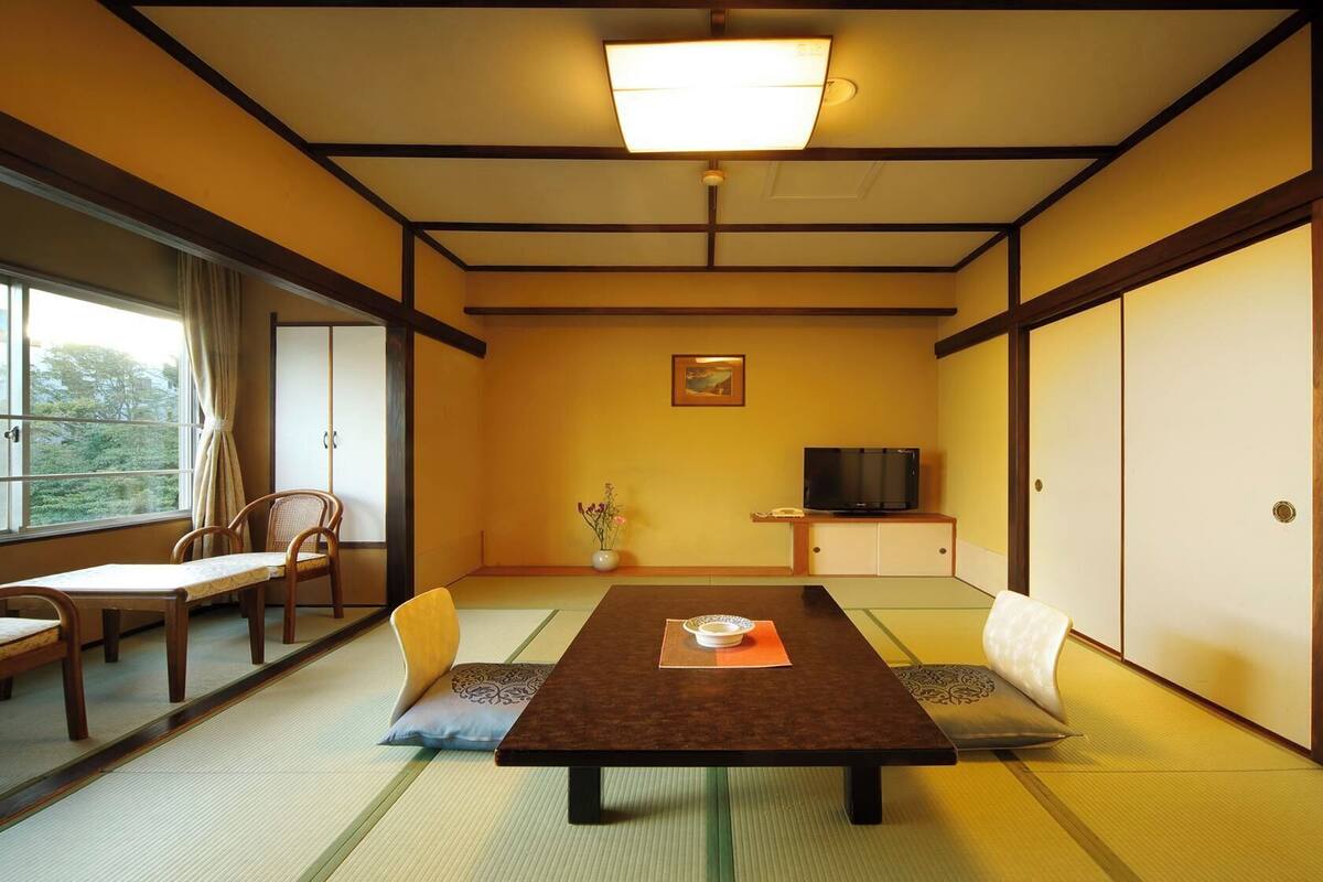 Ein traditioneller japanischer Raum mit Tatami-Böden, einem niedrigen Tisch, Stühlen, einem Fernseher und Schiebetüren.