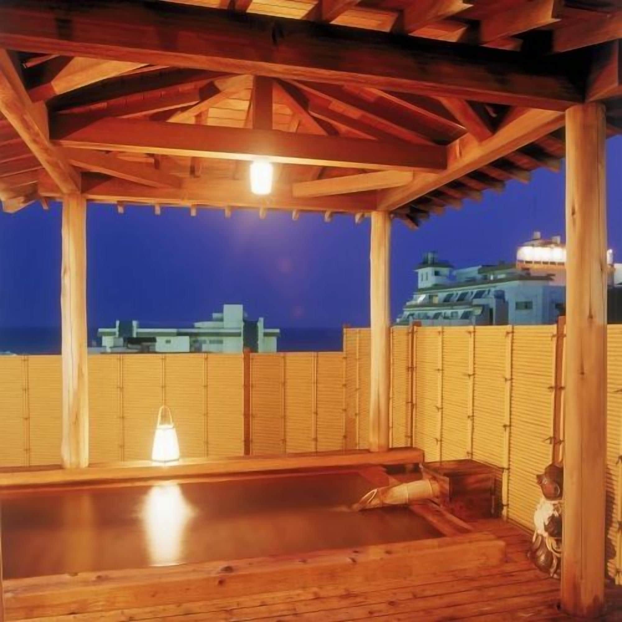 Une terrasse en bois avec un jacuzzi, une clôture en bambou et une vue sur la ville au crépuscule.