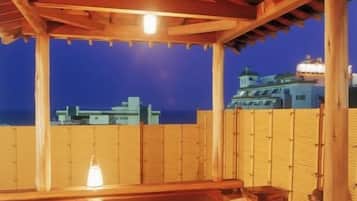 Une terrasse en bois avec un jacuzzi, une clôture en bambou et une vue sur la ville au crépuscule.