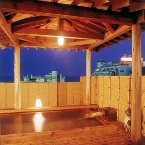 Une terrasse en bois avec un jacuzzi, une clôture en bambou et une vue sur la ville au crépuscule.