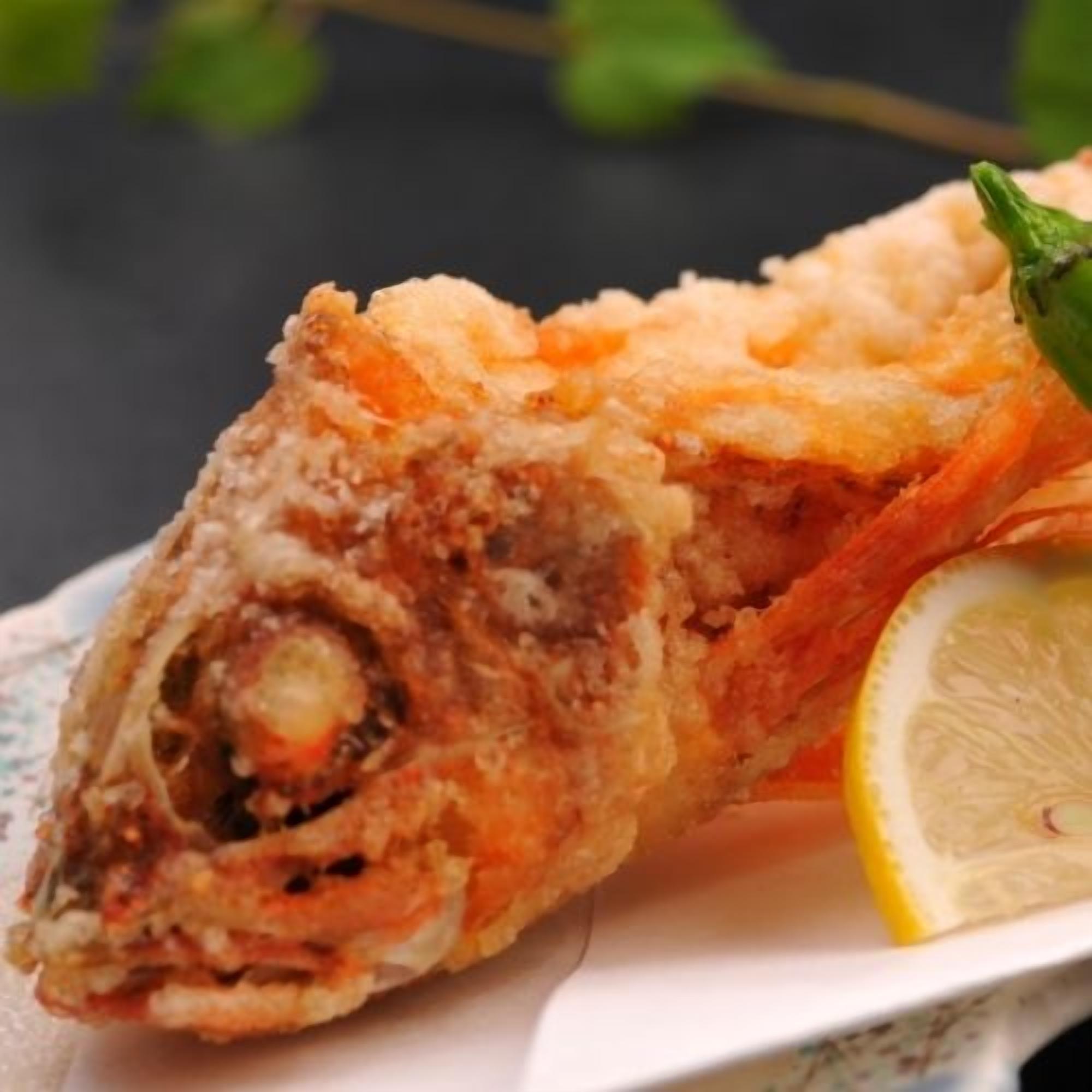 A piece of fried fish with a lemon wedge on a plate.