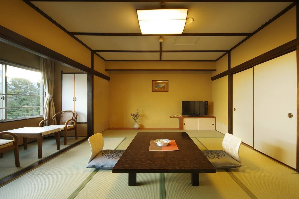 Een traditionele Japanse kamer met tatami vloeren, een lage tafel met kussen, een televisie en schuifdeuren.