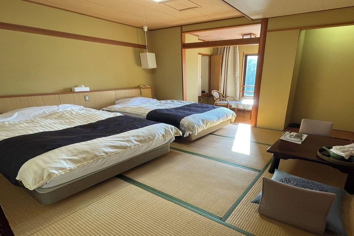 Een hotelkamer met twee bedden, een klein tafeltje met een stoel, een televisie en uitzicht buiten.