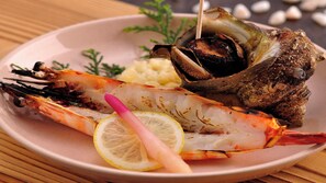 Une assiette avec une crevette grillée, une moule entière et un quartier de citron.