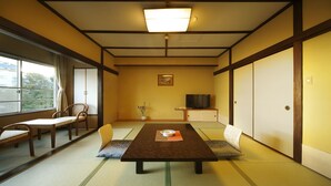 A traditional Japanese room with tatami flooring, a low table with a cushion, a television, and sliding doors. - Aji no Yado Kikuta (Higashiizu)