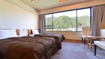 Quarto de hotel com duas camas, vista para as montanhas, uma mesinha e uma cadeira.