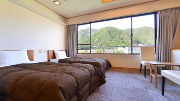 Quarto de hotel com duas camas, vista para as montanhas, uma mesinha e uma cadeira.