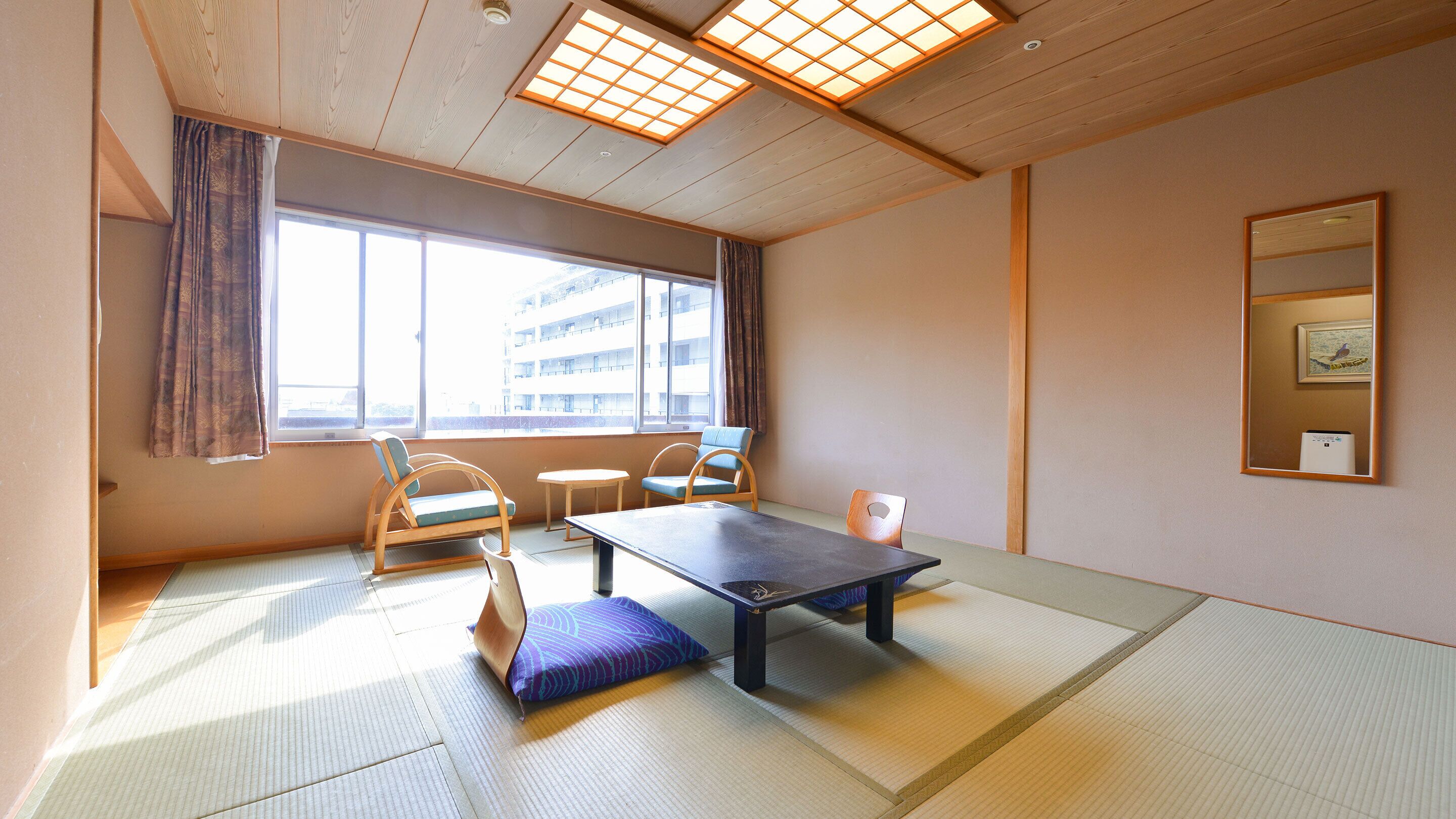 A traditional Japanese room with tatami flooring, a low table, two chairs, and a large window with curtains.